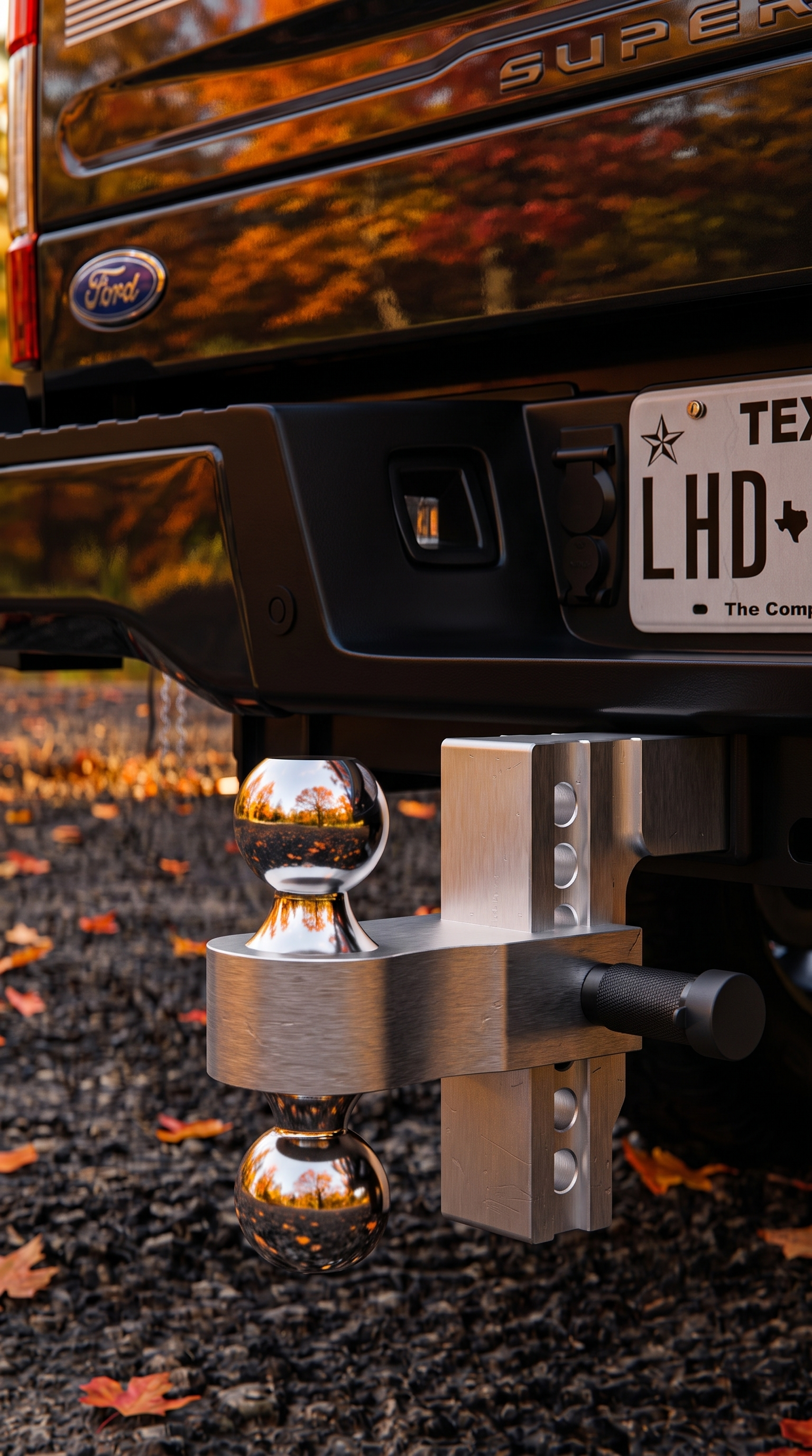 Close-up of the BullBoulder adjustable drop hitch on a black Super Duty, fall leaves on gravel